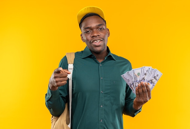 Free photo pleased young afro-american student with cap and backpack holding money and pointing at front