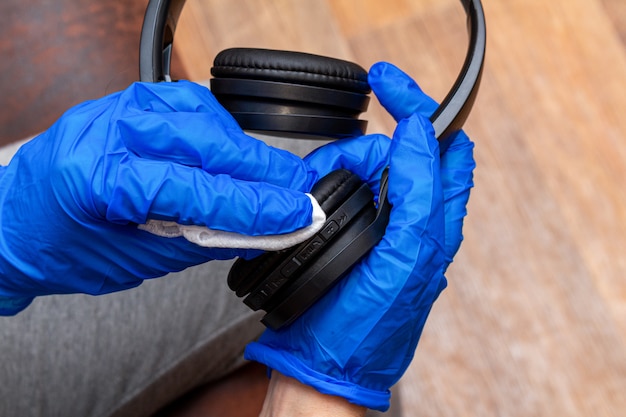 Cleaning, disinfecting, wiping music headphones with a hand in glove and napkin close up